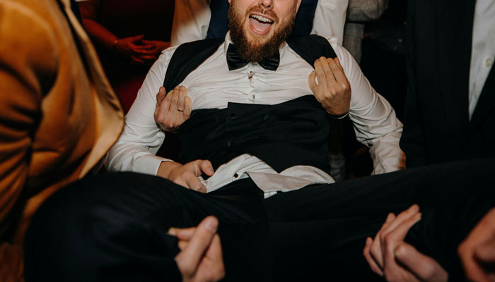 Man in tuxedo being lifted by people at a lively wedding celebration, capturing unexpected moments and wedding regrets. - 4