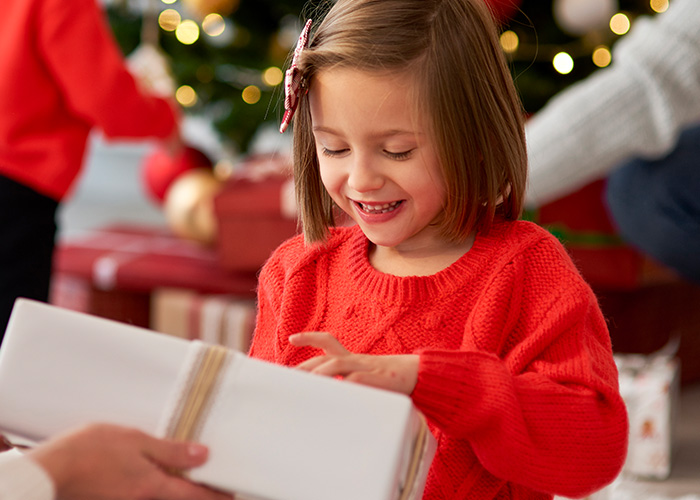 Young girl in a red sweater happily receiving a wrapped gift, capturing the joy parents reveal in hilarious lies to kids.