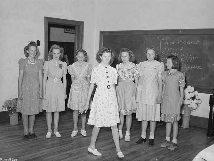Group of young girls in vintage dresses posing in a classroom, showcasing unique old photos with incredible stories behind them.