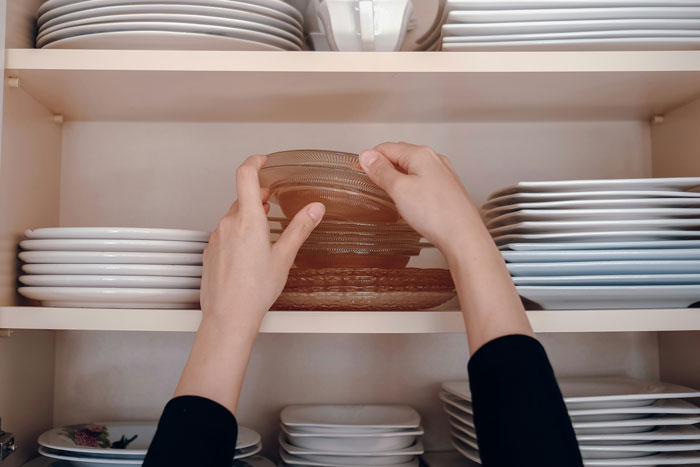 Hands organizing glass plates on a kitchen shelf showing oldschool home trends millennials are absolutely over.