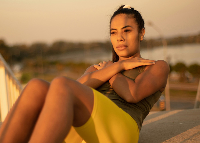 Young woman exercising outdoors at sunset, focused and determined while performing core workout – facts people are tired of explaining.
