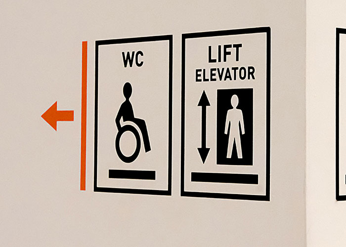 Signage showing wheelchair accessible restroom and elevator directions inside a building with clear icons and arrows.