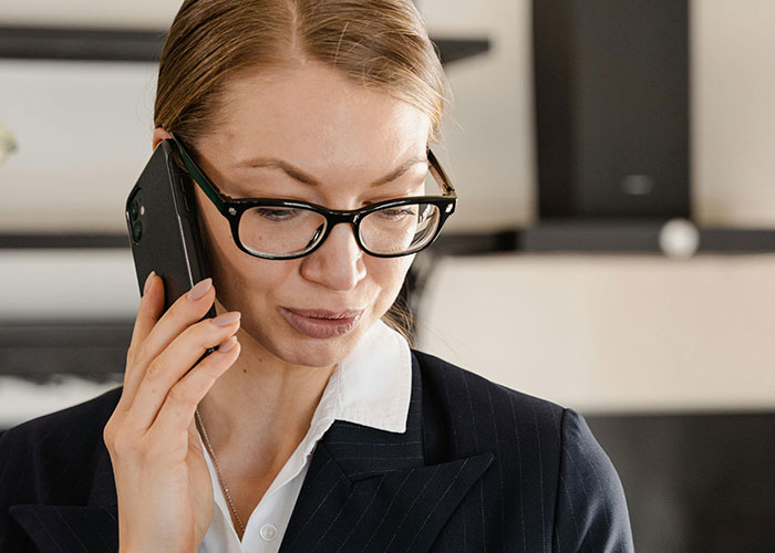 A professional woman wearing glasses and a suit, speaking on the phone, illustrating micromanagement at work.