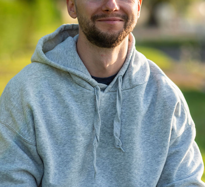 Man in a gray hoodie sitting outdoors, representing scenarios where women share inappropriate comments from men in public spaces.