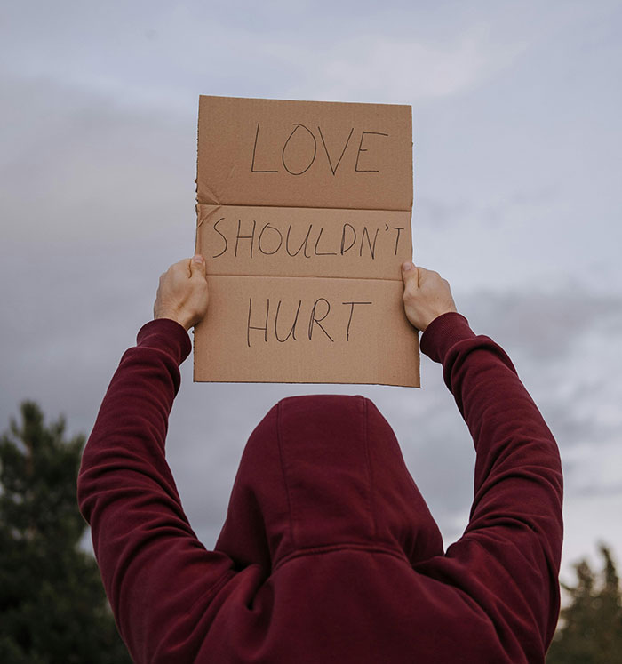 Person in a maroon hoodie holding a sign with love shouldn't hurt message, symbolizing domestic violence awareness and justice.
