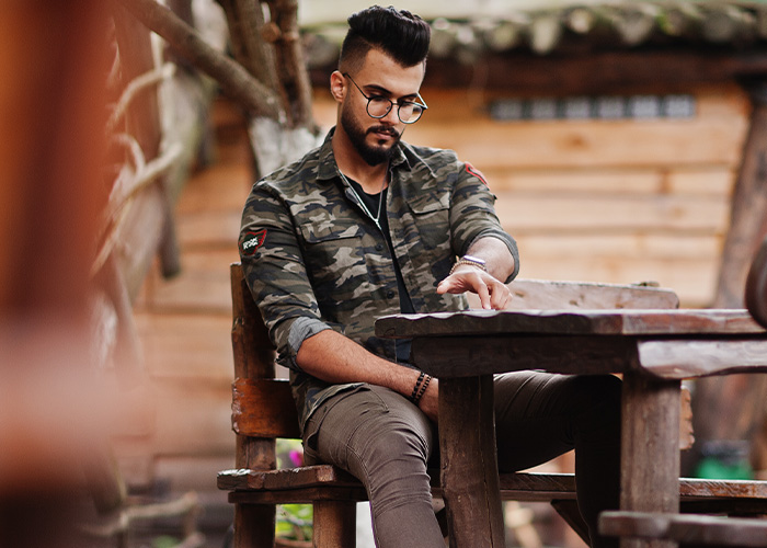 Man with glasses and camouflage jacket sitting outdoors at a wooden table, reflecting on former employee secrets. - 8