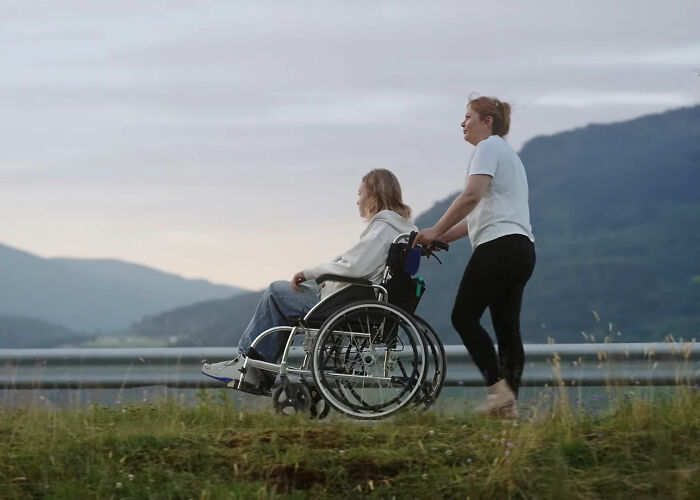 Woman pushing a wheelchair outdoors with a scenic mountain backdrop, symbolizing care after scalping incident in Dubai. - 1