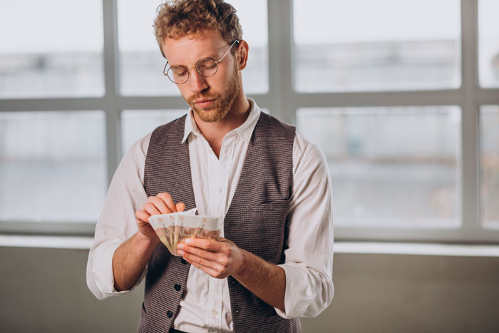 Man in glasses and vest counting money, illustrating unexpected things people learned about the rich after interacting with them.
