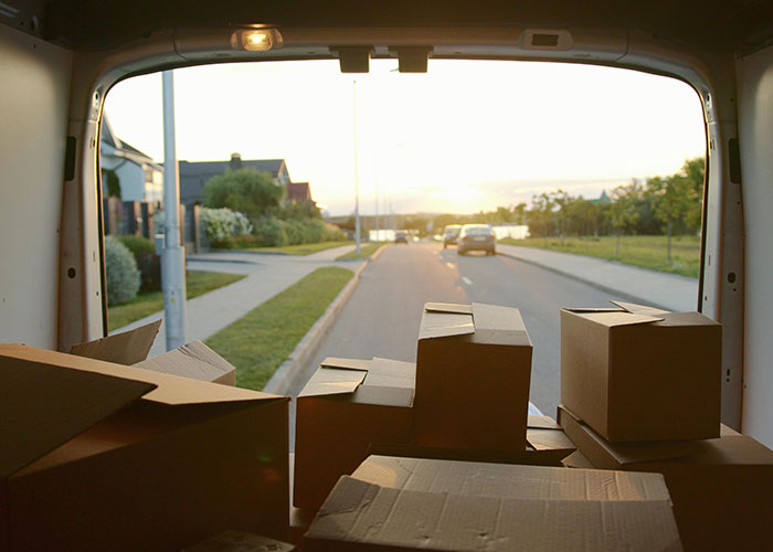 View from inside a moving van filled with packed boxes driving through a suburban neighborhood at sunset.