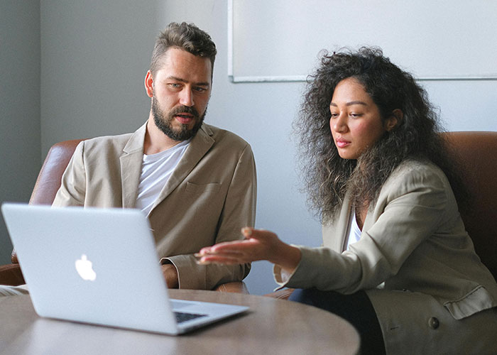 Two coworkers in a meeting discussing work on a laptop, illustrating micromanagement in the workplace environment.