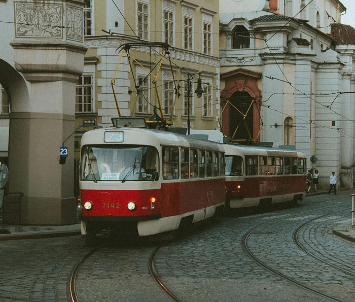 Vintage red tram moving through historic city streets with buildings in the background and few pedestrians nearby