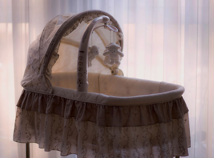 Empty vintage baby bassinet with hanging toys in dim light, evoking real-life horror stories and unexplainable events. - 7