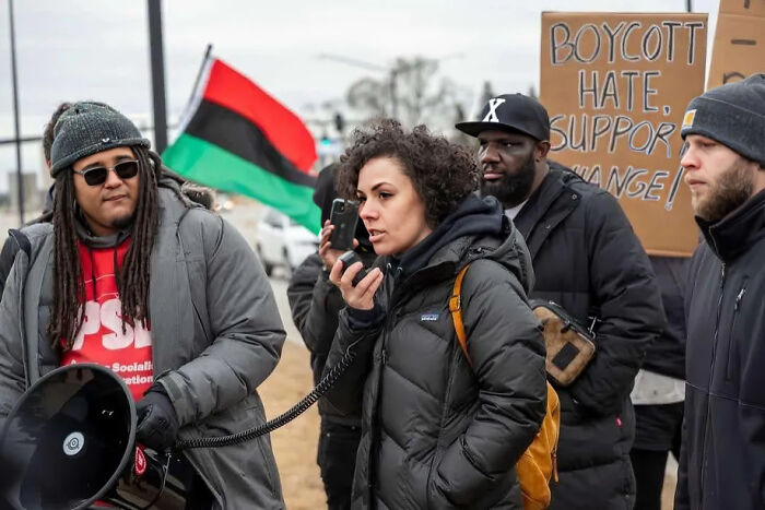 Protesters using a megaphone and holding signs, illustrating consequences of their own actions leading to job loss.