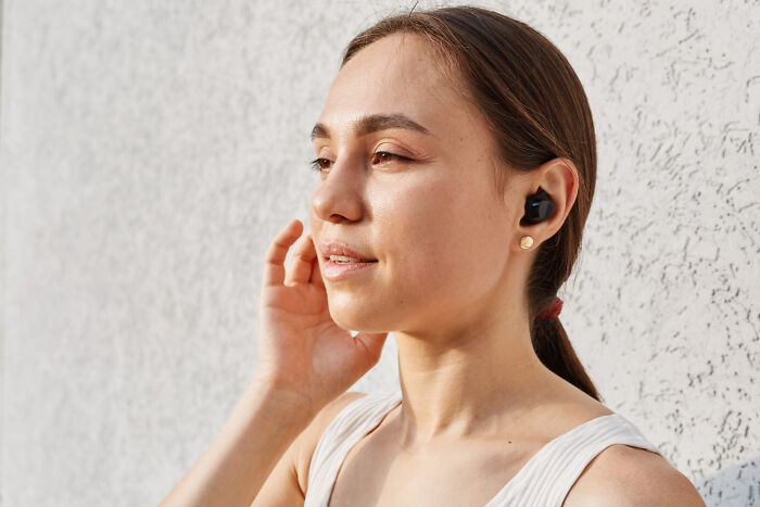 Young woman wearing wireless earbuds, touching ear, illustrating normal people's habits some netizens find creepy. - 28