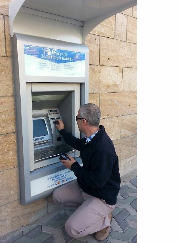 Man kneeling to use an ATM installed too low on a wall, showcasing a home creativity fail in design and placement.