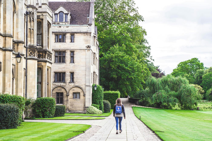 Person walking on a paved path near a large historic mansion and manicured gardens learning about the rich lifestyle.