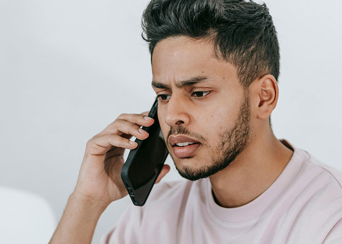 Young man with worried expression talking on phone, reflecting tension from worst cheating stories.