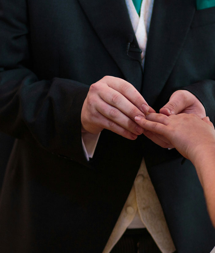 Close-up of a groom wearing a suit placing a ring on a bride’s hand during a wedding ceremony related to women who married rich.