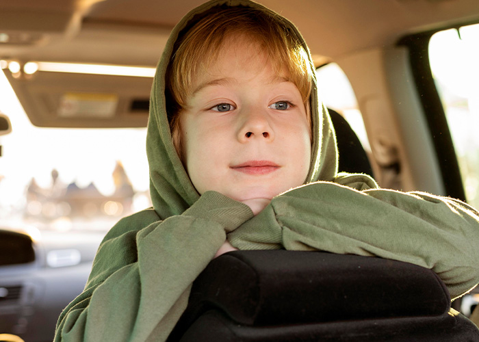 Child wearing a green hoodie sitting in a car looking thoughtful, representing parents revealing hilarious lies to kids.