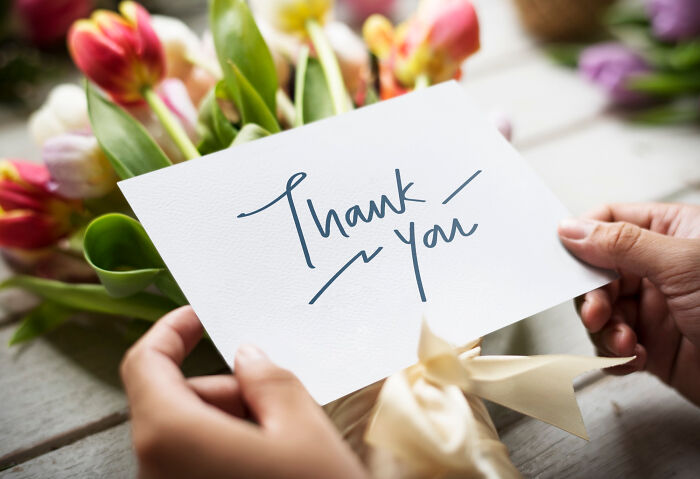 Person holding a thank you note with flowers in the background, symbolizing thank you notes from the past.