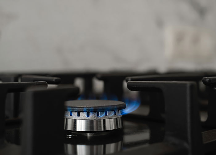 Close-up of a gas stove burner with blue flame, illustrating tips to stay safe and alive while cooking at home.