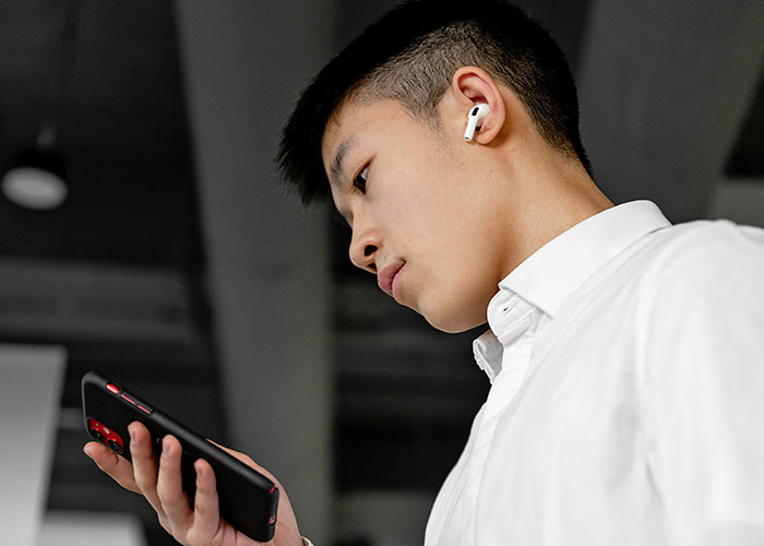 Young man wearing wireless earbuds looking at phone with concerned expression, illustrating cheating stories theme