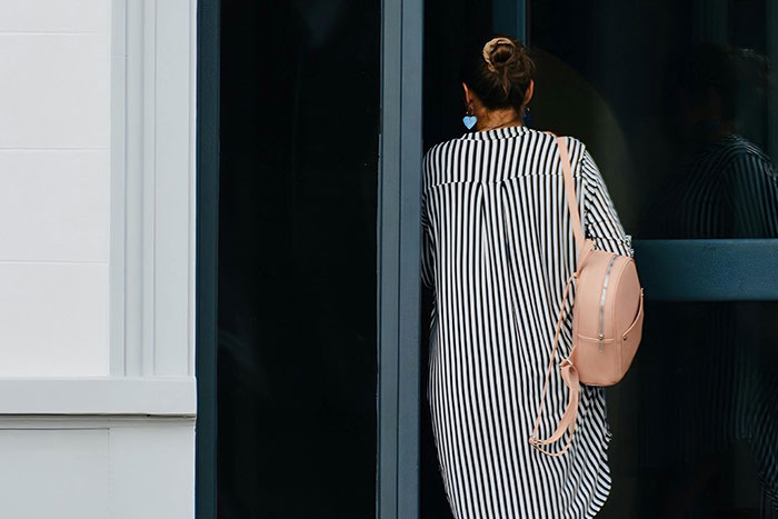 Woman in a striped dress holding a door open, illustrating themes related to microfeminisms and social interactions.