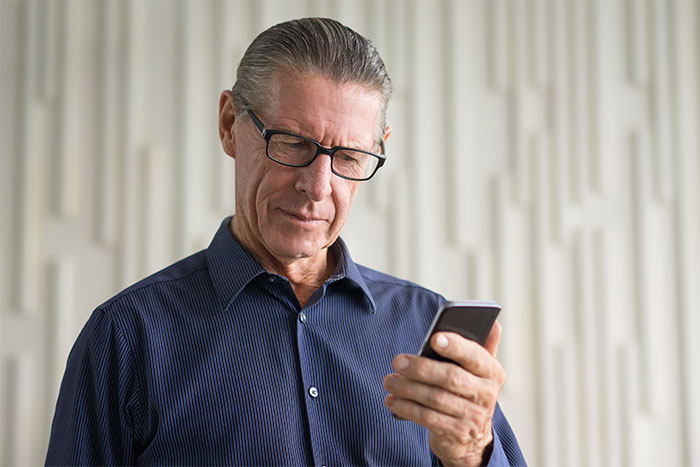 Older man with glasses looking seriously at a smartphone, portraying a dad receiving important news from woman.