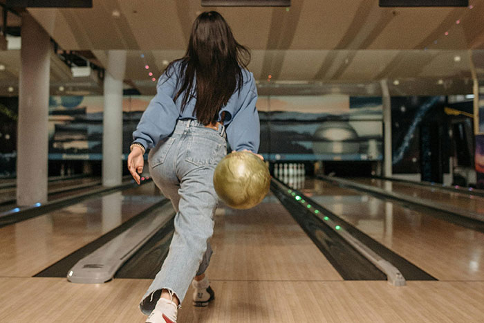 Woman bowling at an indoor alley, focusing on her throw, illustrating microfeminisms in a casual setting.