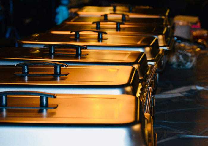 Row of closed buffet trays with warm lighting, representing catering at a wedding event with people regretting attendance. - 15