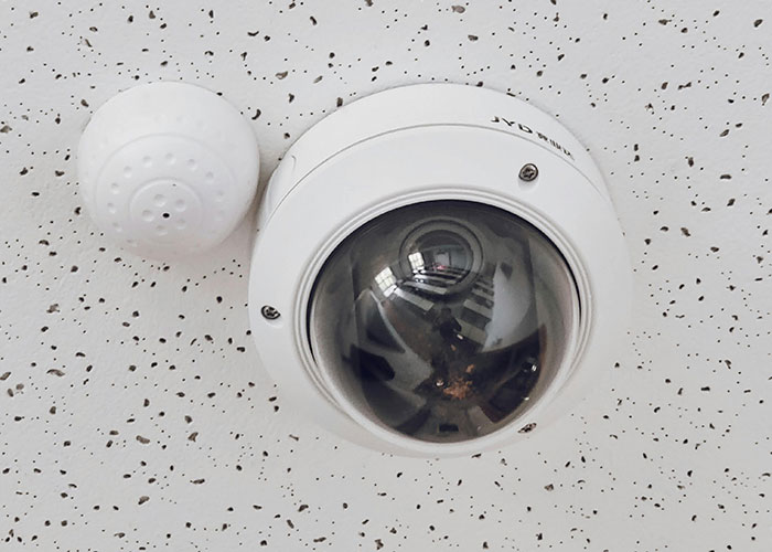 Ceiling security camera and sensor installed on a white speckled ceiling, related to bizarre family behaviors surveillance.
