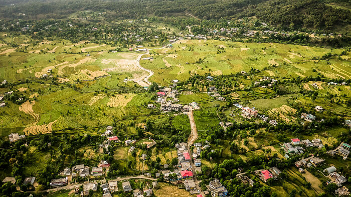 Aerial view of a rural landscape showing effects of natural disasters with scattered houses and green fields.