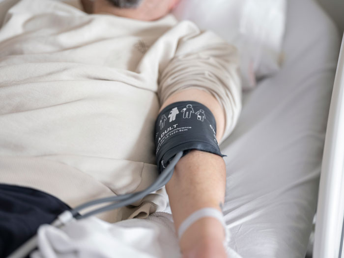Patient lying in hospital bed with blood pressure cuff on arm, highlighting common hospital mistakes risks.