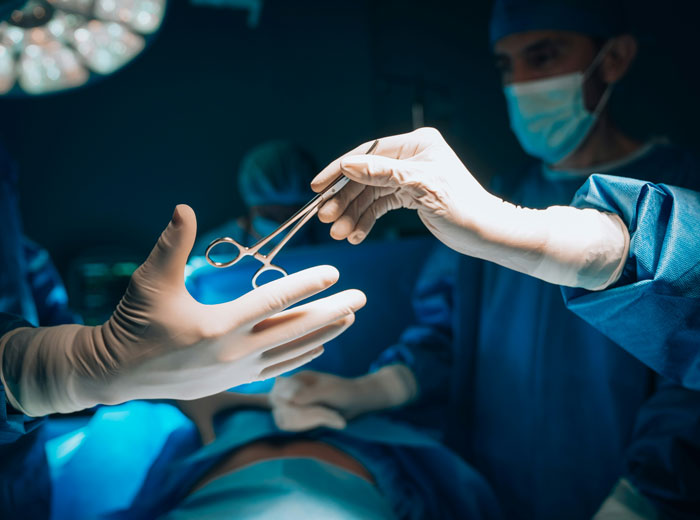 Surgeons in sterile gloves passing surgical tools during a procedure highlighting hospital mistakes risk.