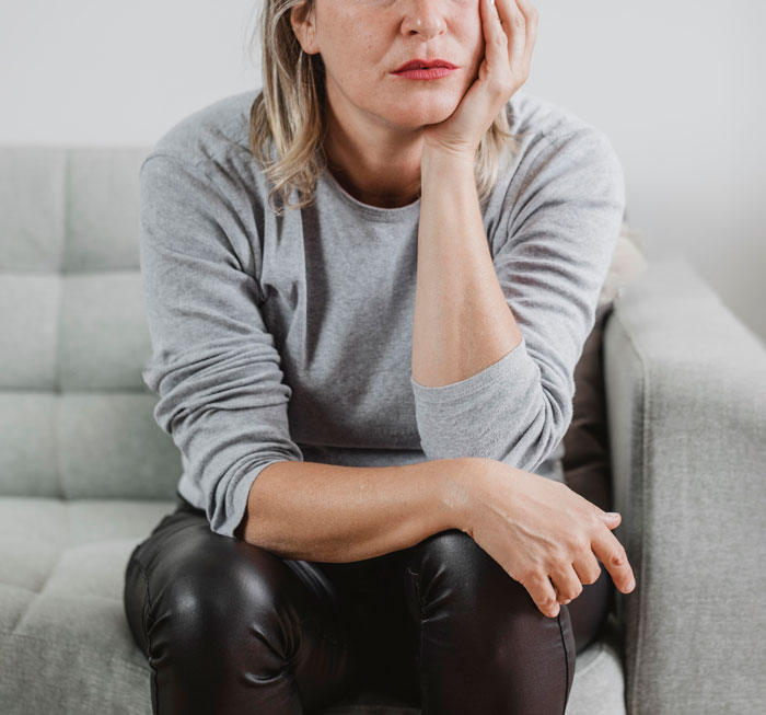 Middle-aged woman sitting thoughtfully on a couch, illustrating therapists share differences between men and women. - 3