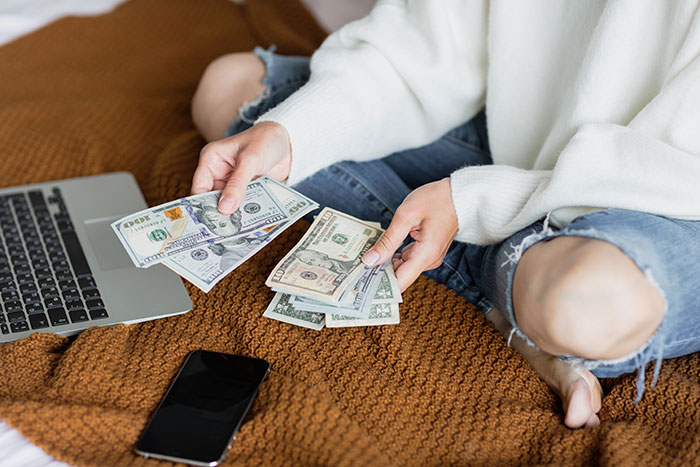 Person counting cash near laptop and smartphone, illustrating husband promises daughter's inheritance to freeloader sister conflict. - 9