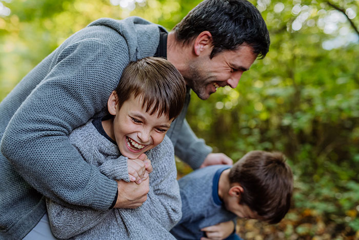 Man happily playing outdoors with children, symbolizing partner caring for children from other men in complex family dynamics