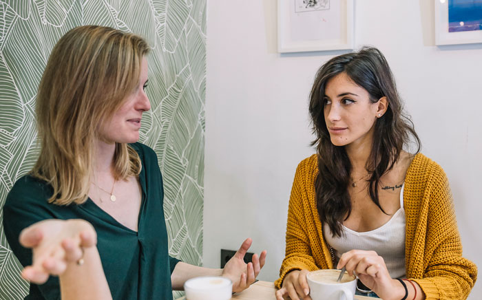 Two women having a serious discussion over coffee indoors, illustrating a nanny asked to work overnight for limited pay. - 5