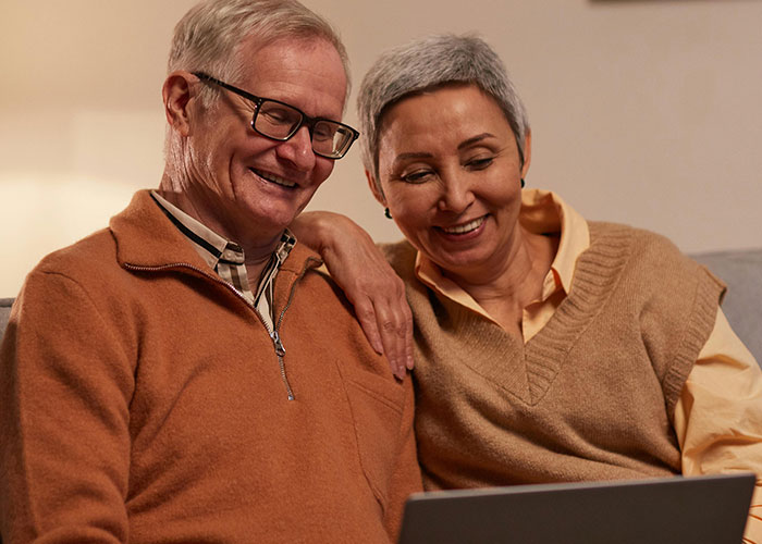 Older couple smiling and watching a laptop together, discussing modern parents and mixed reactions online. Older couple smiling and watching a laptop together, discussing modern parents and mixed reactions online.