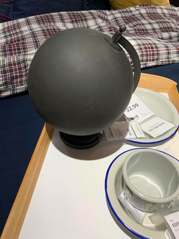Black globe with no visible map details displayed on a table with bed textiles and dishware nearby.