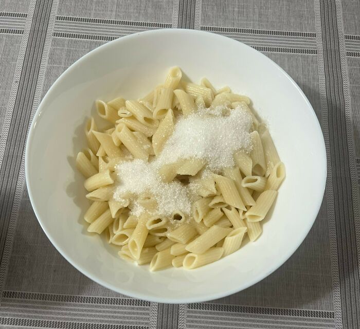 Bowl of plain cooked penne pasta topped with granulated sugar, illustrating bizarre facts about countries' unique food customs.