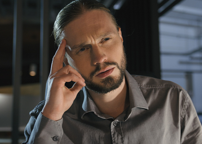 Man in gray shirt with beard and long hair, looking confused while thinking about ridiculous employee complaints to managers and HR.