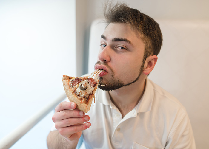 Man eating pizza slice with melted cheese stretching, illustrating facts people are tired of explaining to others.