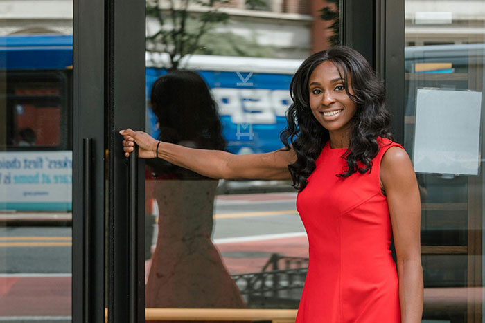Woman in a red dress holding a door open on a city street, illustrating microfeminisms and social interactions.