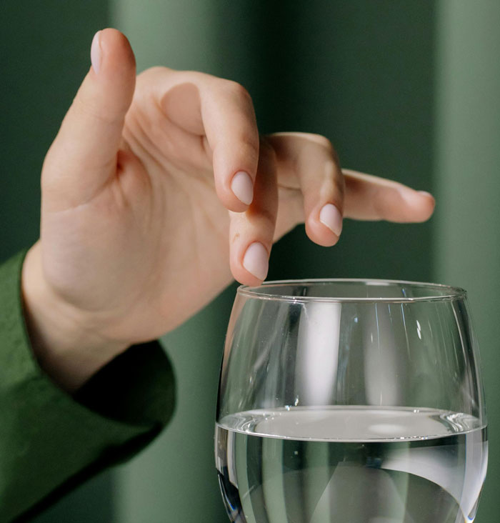 Close-up of a person’s hand about to tap on a glass of water, representing women sharing inappropriate comments in public spaces