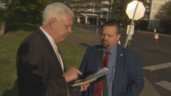 Two men in suits discussing documents outdoors, illustrating consequences of workplace mistakes and lost jobs.