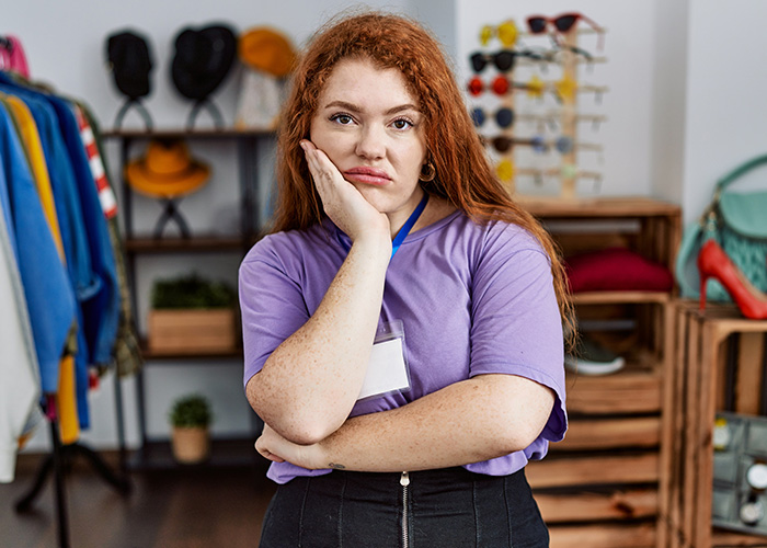 Former employee with red hair wearing a purple shirt, looking frustrated while standing in a retail store environment. - 9