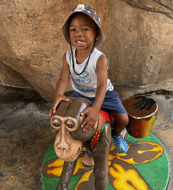 3-year-old boy in temporary foster care smiling while sitting on a monkey statue in a playful setting - 11