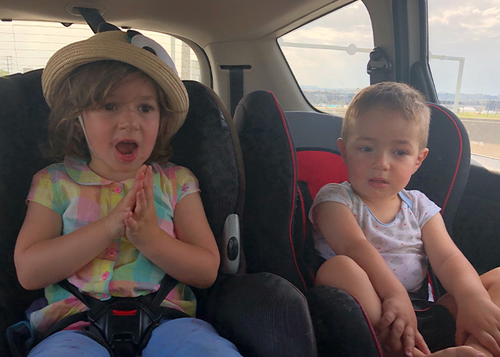 Two young kids in car seats with expressive faces, illustrating parents’ hilarious lies they tell their kids.