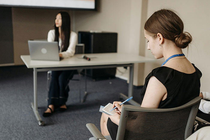 A woman attentively taking notes during a discussion on microfeminisms in a modern conference room setting.